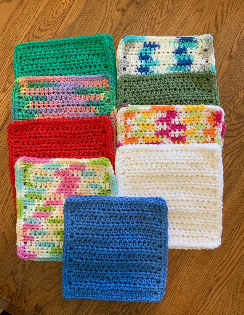 May include: A collection of nine square crochet washcloths arranged in a grid. The set includes solid colors in green, red, white, and blue, alongside variegated patterns featuring combinations of pink, yellow, blue, green, and white yarn textures.