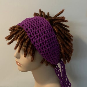 May include: Purple crochet headband with a tie at the back. The headband is worn on a mannequin with brown dreadlocks.