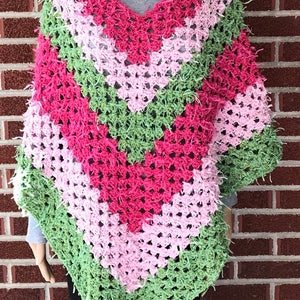 Pode incluir: Um poncho de crochê com decote em V e um padrão listrado em tons de rosa, verde e branco.