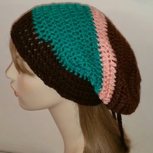 Peut inclure: Un bonnet crocheté marron, turquoise et rose avec une longue ficelle marron.
