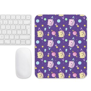 May include: A purple mousepad with a repeating pattern of cartoon planets, stars, and bear-like characters. The mousepad is next to a white keyboard and mouse. The planets have rings and the stars are yellow.