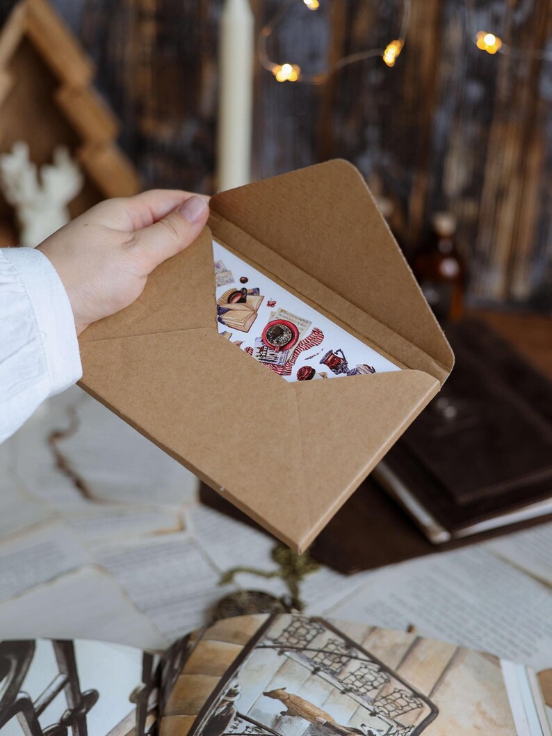 K&ouml;nnte beinhalten: Ein brauner Kraftpapierumschlag enth&auml;lt eine Karte mit verschiedenen Aufklebern. Die Karte zeigt Bilder von Kaffee, B&uuml;chern und Elementen zum Thema Vintage. Die Szene spielt auf einem Tisch mit verstreuten Papieren und einem unscharfen Hintergrund.