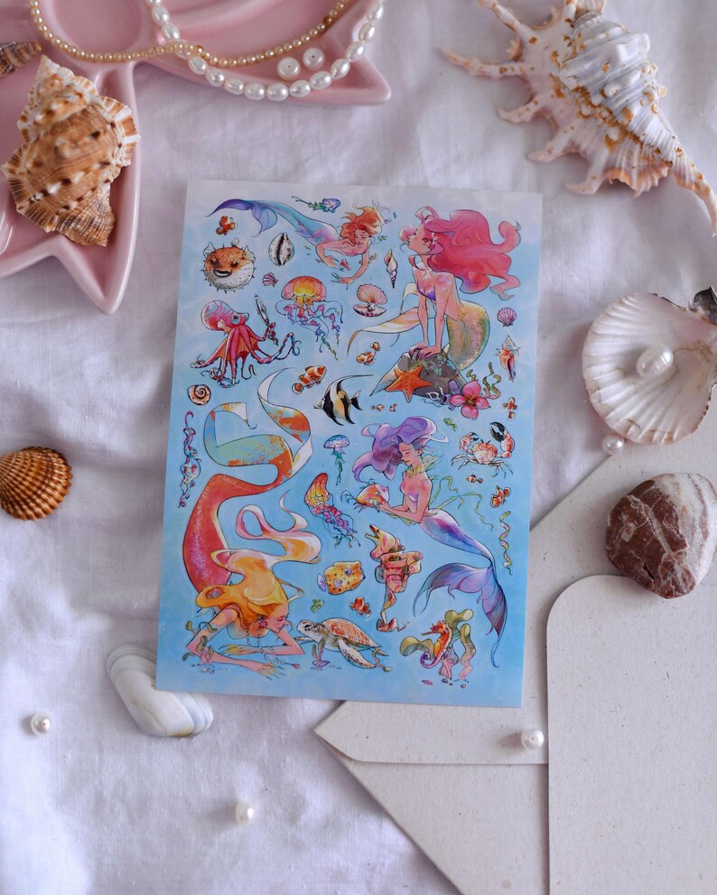 Puede incluir: Una hoja de pegatinas con ilustraciones de sirenas y criaturas marinas. El dise&ntilde;o incluye sirenas con pelo rosa, morado y naranja, junto con peces, medusas y otra vida marina. El fondo es de color azul claro.