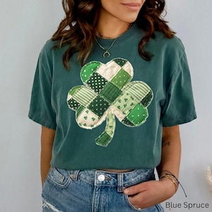Op de afbeelding: Een tealkleurig T-shirt met een patchwork klaverontwerp in verschillende tinten groen en wit. De klaver staat centraal op het shirt, met de tekst "Blue Spruce" onderaan.