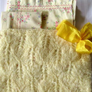 May include: A soft, yellow knitted blanket with a delicate, lacy pattern. The blanket is folded in half and has a yellow satin ribbon tied around it.