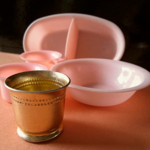 May include: A set of pink plastic bowls and a gold metal cup. The bowls are divided into sections and are perfect for serving snacks or dips. The cup is a classic design with a beaded rim.