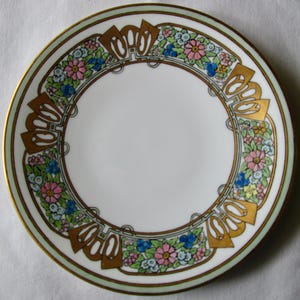 May include: A white porcelain plate with a decorative floral border. The border features pink, blue, and yellow flowers with gold accents and a light green rim. The plate has a gold trim.