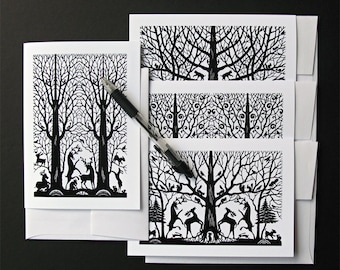 May include: Set of four black and white greeting cards featuring a silhouette design of a forest with trees, birds, and deer. The cards are blank inside for writing a message.
