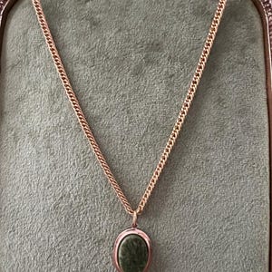 May include: A gold chain necklace with a green oval pendant. The pendant is set in a gold frame.