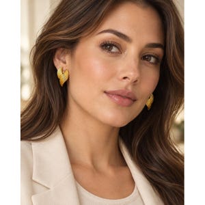 May include: A pair of gold-toned earrings featuring a ribbed, fan-like design with curved, layered segments. The earrings have a polished metallic finish and a structured, dimensional shape that tapers toward the bottom, creating a distinct texture.