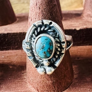May include: A silver ring with a turquoise stone. The ring has a detailed, ornate design around the stone, with a leaf-like pattern. The turquoise stone is oval-shaped and set in a silver bezel.