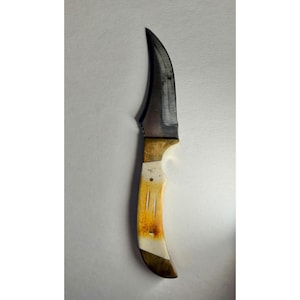 May include: A fixed-blade knife featuring a curved, dark steel blade with a visible metallic grain. The handle is constructed from a combination of smooth, cream-colored bone and dark, polished wood accents, secured with a single visible metal pin.