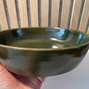 Peut inclure: Un grand bol en céramique vert foncé avec une finition brillante. Le bol est rond et a un bord large.