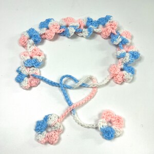 Puede incluir: Una guirnalda de flores de ganchillo con flores rosas, azules y blancas. La guirnalda tiene una larga corbata que se puede usar para ajustar la longitud.