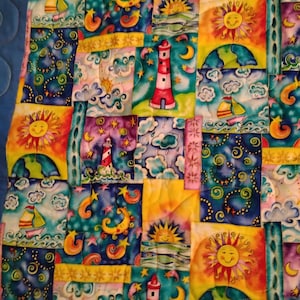 May include: A patchwork quilt featuring a repeating pattern of nautical and celestial motifs, including red and white lighthouses, yellow smiling suns, crescent moons, sailboats on blue waves, and starry night skies in vibrant shades of blue, yellow, and purple.