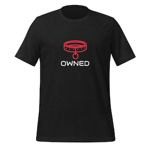 Può includere: T-shirt nero con un contorno rosso di un collare per cani e la parola "OWNED" in testo bianco.