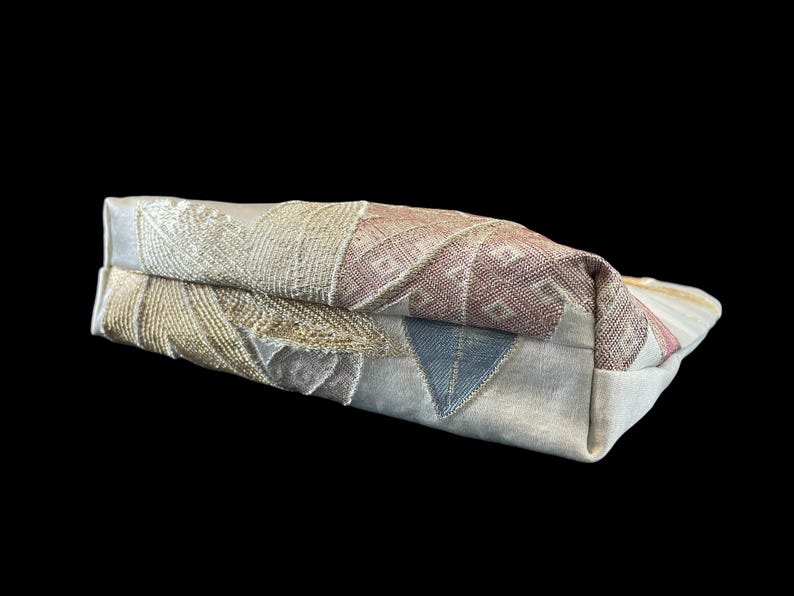 May include: A beige fabric clutch bag with a colorful embroidered design featuring geometric shapes and floral patterns.