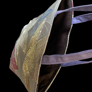 May include: A brown tote bag with a gold and purple design. The bag has a purple strap and a brown lining.