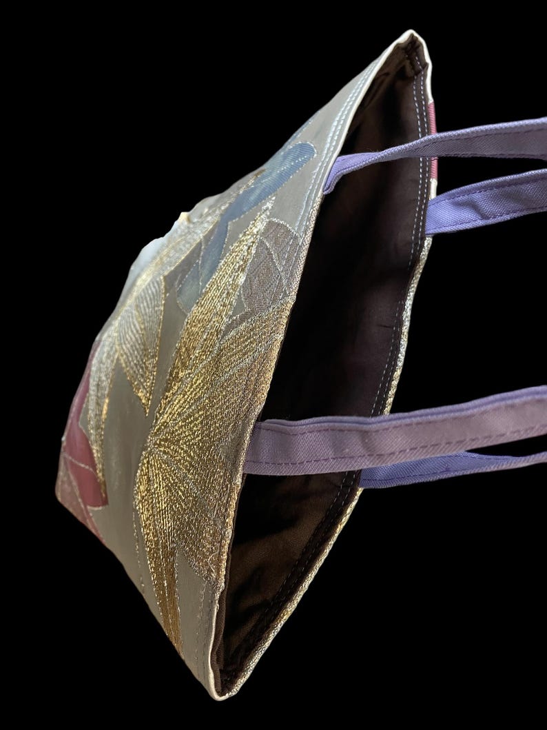 May include: A brown tote bag with a gold and purple design. The bag has a purple strap and a brown lining.