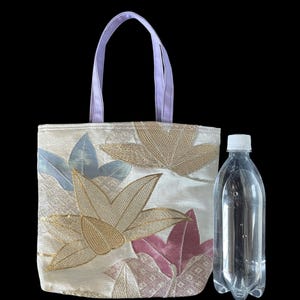 May include: A small, white tote bag with a floral design featuring pink, gold, and blue flowers. The bag has lavender handles and is made of a textured fabric.