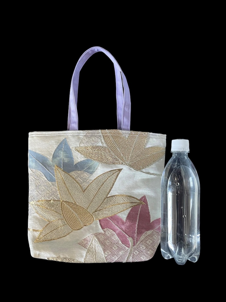 May include: A small, white tote bag with a floral design featuring pink, gold, and blue flowers. The bag has lavender handles and is made of a textured fabric.