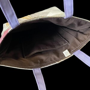 May include: A purple and white tote bag with a brown fabric lining. The bag has a small pocket on the inside and a label with the text "CJ".