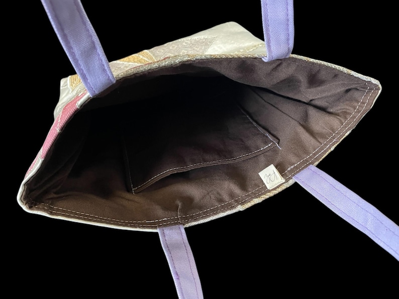 May include: A purple and white tote bag with a brown fabric lining. The bag has a small pocket on the inside and a label with the text "CJ".
