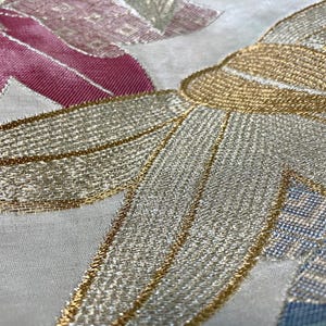 May include: Close-up of a white fabric with gold and silver embroidery. The embroidery features a floral design with intricate details.