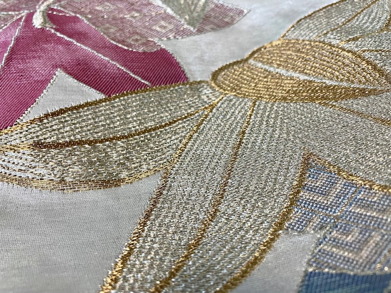 May include: Close-up of a white fabric with gold and silver embroidery. The embroidery features a floral design with intricate details.
