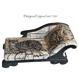 May include: A decorative miniature chaise lounge with a cat illustration. The black and white artwork features a tabby cat reclining on the seat. The text "Original signed art 1991" is written above the chaise lounge.