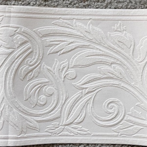 Puede incluir: Borde de papel pintado blanco en relieve con un patrón repetido de hojas estilizadas y vides arremolinadas. El diseño está en relieve, creando un efecto texturizado. El borde es rectangular.
