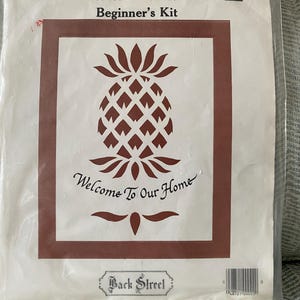 May include: A clear plastic package containing a Scherenschnitte Beginner's Kit. The kit features a brown pineapple design with the text "Welcome To Our Home." The package also includes the text "Scissors' Cuttings" and "Back Street."