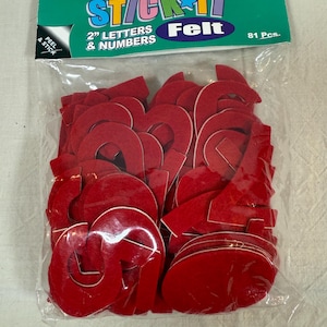 May include: A clear plastic bag containing 81 pieces of red felt letters and numbers. The package reads "STICK IT Felt" and "2" LETTERS & NUMBERS". The felt letters and numbers are adhesive-backed.