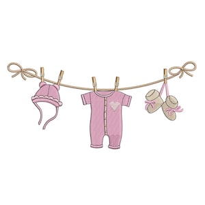 Puede incluir: Ropa de bebé rosa colgada de una cuerda para tender la ropa con pinzas. La ropa incluye un gorro, un mono y botines.
