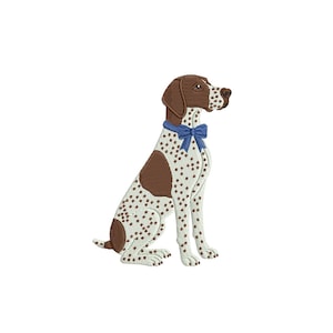May include: An embroidered patch featuring a sitting dog with a brown head, ears, and large spots on its body. The dog has a white coat with brown speckles and wears a bright blue bow tie around its neck. The design is rendered in detailed stitching.