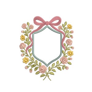 May include: An embroidered floral crest design featuring a light blue shield shape, surrounded by pink roses, yellow flowers, and green leaves. A pink ribbon bow adorns the top. The design is on a white background.