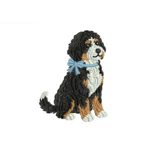 May include: Embroidered image of a Bernese Mountain Dog puppy, featuring black, white, and tan fur. The dog is seated and wears a light blue bow around its neck. The image is detailed and suitable for various craft projects.