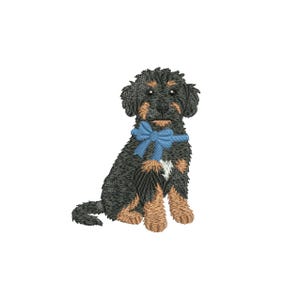 Peut inclure: Un motif brodé représentant un chiot noir et feu assis. Le chiot porte un nœud bleu clair autour du cou et possède une petite tache de poils blancs sur la poitrine. La broderie présente des points détaillés pour représenter la texture du poil.