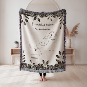 Puede incluir: Una manta tejida beige con un borde floral y el texto "Friendship knows no distance". La manta presenta contornos de mapas con chinchetas y nombres, y el a&ntilde;o "Est.2015."