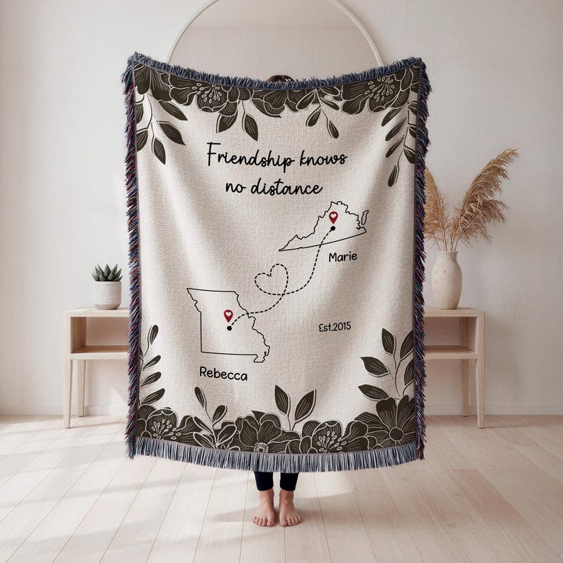 Puede incluir: Una manta tejida beige con un borde floral y el texto "Friendship knows no distance". La manta presenta contornos de mapas con chinchetas y nombres, y el a&ntilde;o "Est.2015."