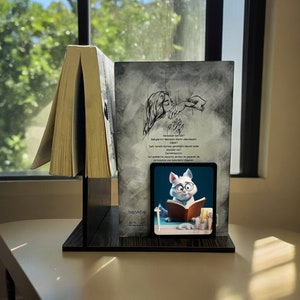 Può includere: Un fermacarte nero con uno sfondo grigio che presenta una mano tesa. Il fermacarte ha una piccola immagine in bianco e nero di un gatto che legge un libro. Il testo sul fermacarte dice "Hayy'kitap 20 TL."