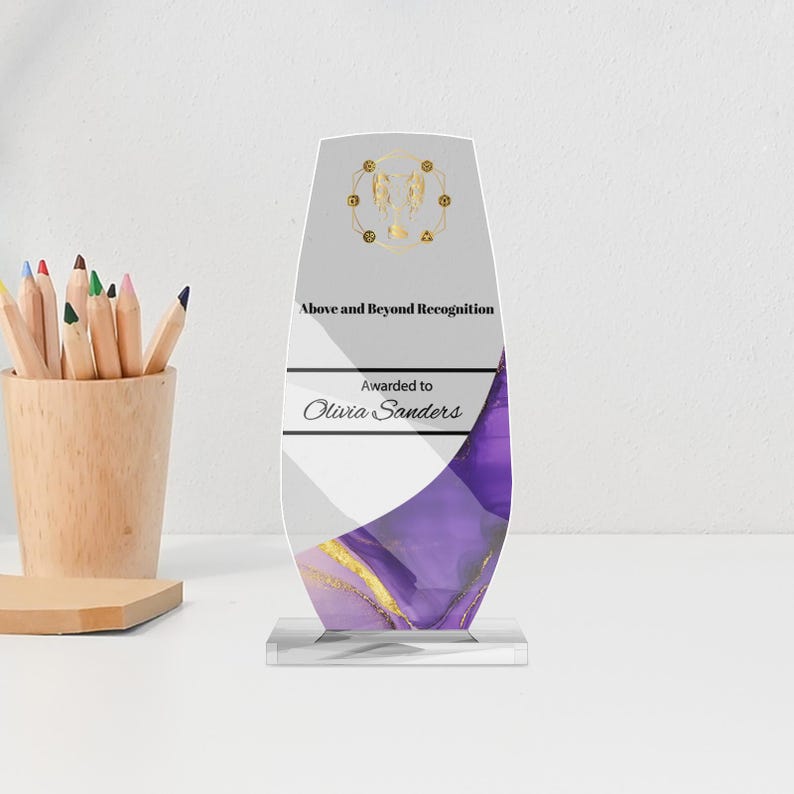 May include: A clear acrylic award with a white and purple marbled design, gold accents, and the text "Above and Beyond Recognition." The award is inscribed "Awarded to Olivia Sanders."