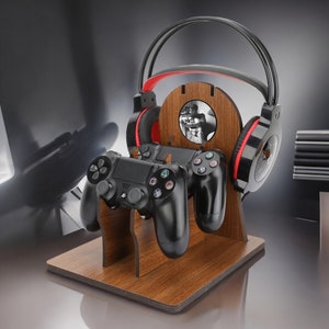 May include: A wooden stand with a headset holder and two slots for video game controllers. The stand has a brown wood finish and a black headset with red accents. The controllers are black and have a PlayStation logo.