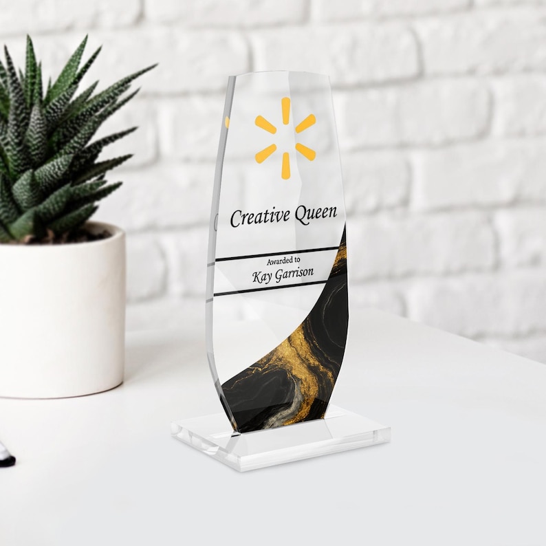May include: A clear acrylic award with a yellow starburst logo and the words "Creative Queen" and "Awarded to Kay Garrison." The base features a black and gold marbled design.