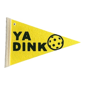 May include: Yellow pennant with the words "YA DINK" in black, along with a black pickleball graphic. The pennant has a white border and a small grommet at the top. The pennant is made of felt.