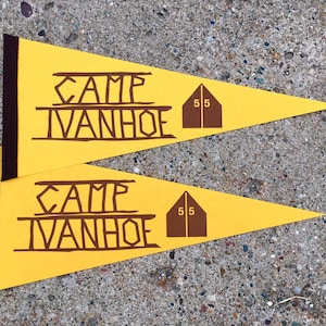 May include: Two yellow pennants with brown text and a brown tent graphic. The text on the pennants reads "Camp Ivanhoe" and "55".