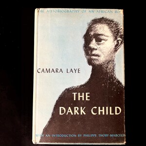 May include: The cover of a book titled "The Dark Child" by Camara Laye. The cover features a black and white illustration of a young person's face. The text "The Autobiography of an African Boy" is printed at the top of the cover.