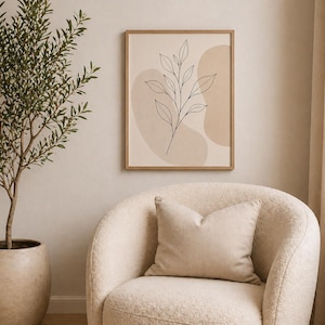 Puede incluir: Un estampado botánico enmarcado con un diseño minimalista que presenta un dibujo lineal negro de una planta con hojas. El estampado cuelga sobre un sillón color crema con un cojín a juego. A la izquierda hay un olivo en maceta.