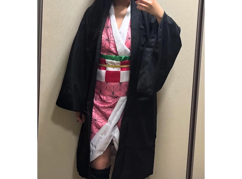 May include: A cosplay costume with a black overcoat, a pink patterned kimono, and a red and white checkered obi belt. The costume has a white collar and accents, with a green and gold belt. The outfit is designed for cosplay events.