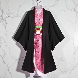May include: A black kimono-style robe with wide sleeves, layered over a pink patterned garment. The pink garment features a geometric design. A colourful obi belt with red, white, and green accents cinches the waist. The outfit is displayed on a hanger.